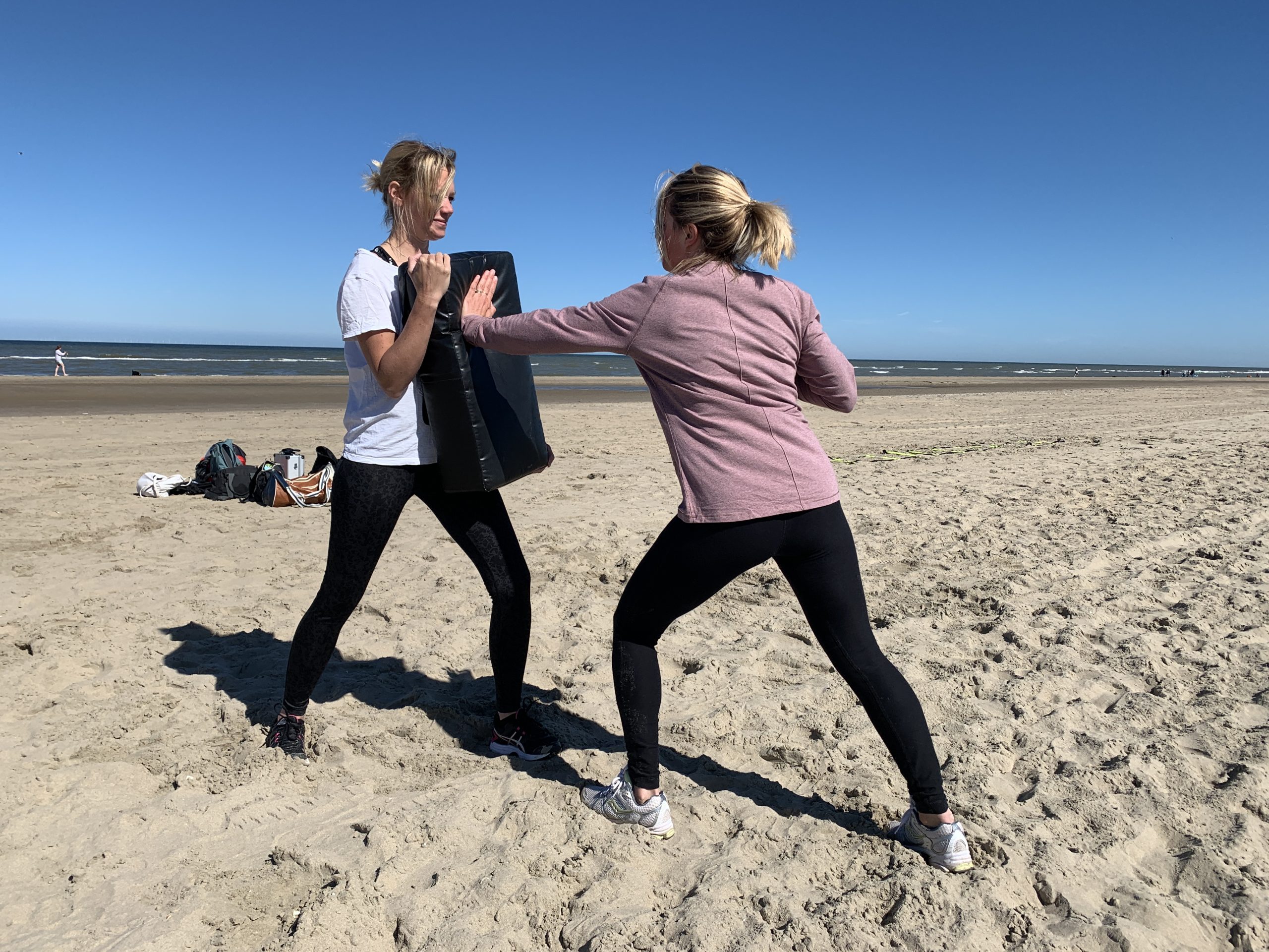 Bootcamp Weerbaarheid & Zelfverdediging 21 Twee vrouwen op het strand slaan tegen een kussen tijdens de Bootcamp Weerbaarheid en Zelfverdediging